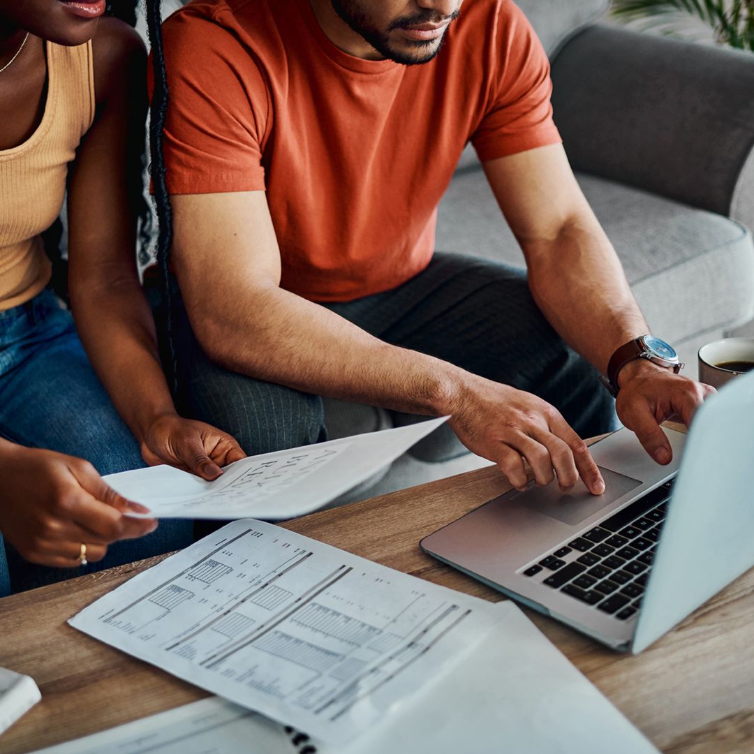 Man and woman sitting on the couch reviewing bills and working on a laptop