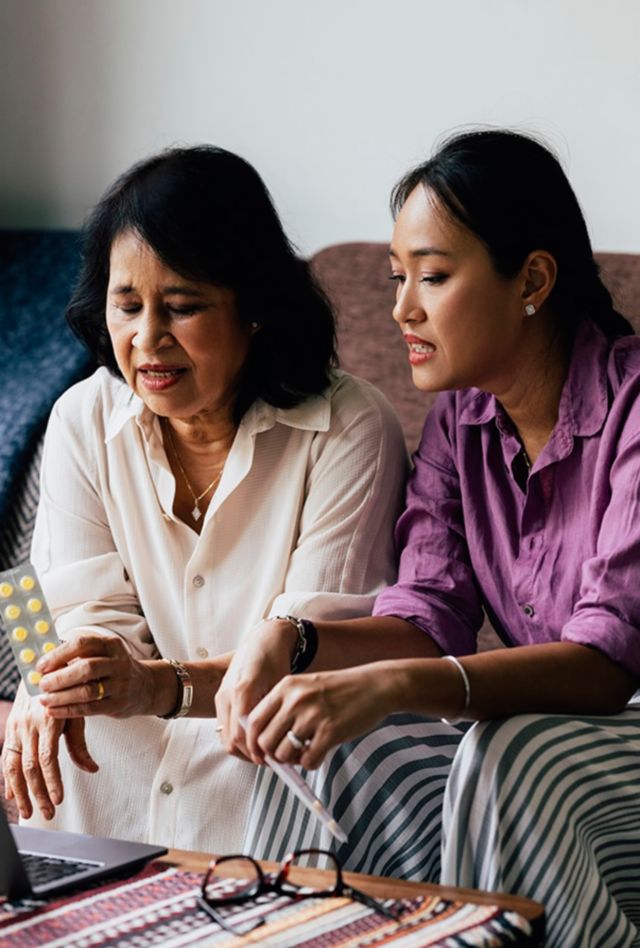Senior woman showing her pills to a doctor at an online appointment while her daughter is sitting next to her.