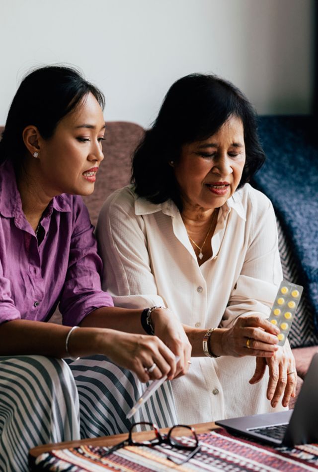 Senior woman showing her pills to a doctor at an online appointment while her daughter is sitting next to her.