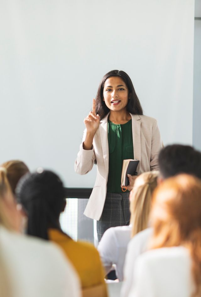 A diverse businesswoman leads a seminar in a bright, naturally-lit conference room.