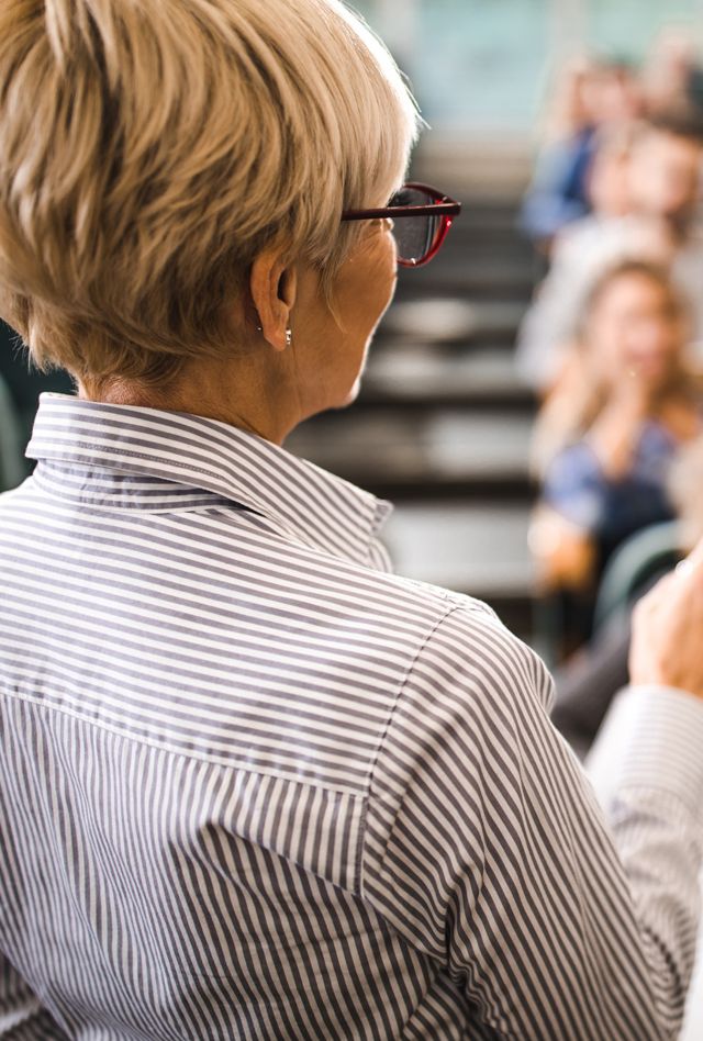 Back view of a senior professor talking on a class to large group of students.