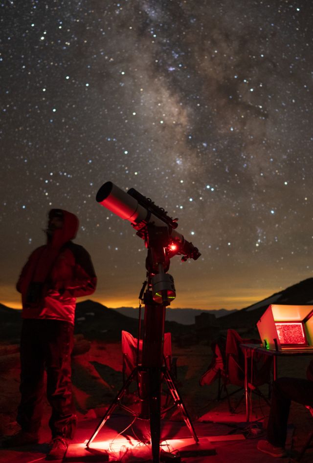 Two people silhouetted against the night sky with a large telescope and other equipment