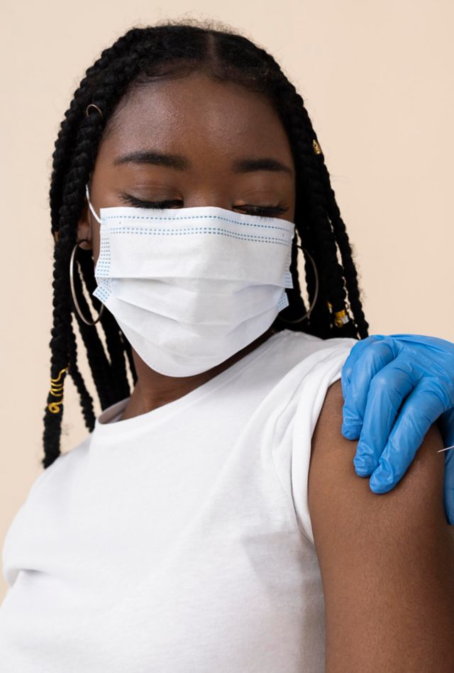 A young black woman in a mask gets a vaccine in the arm