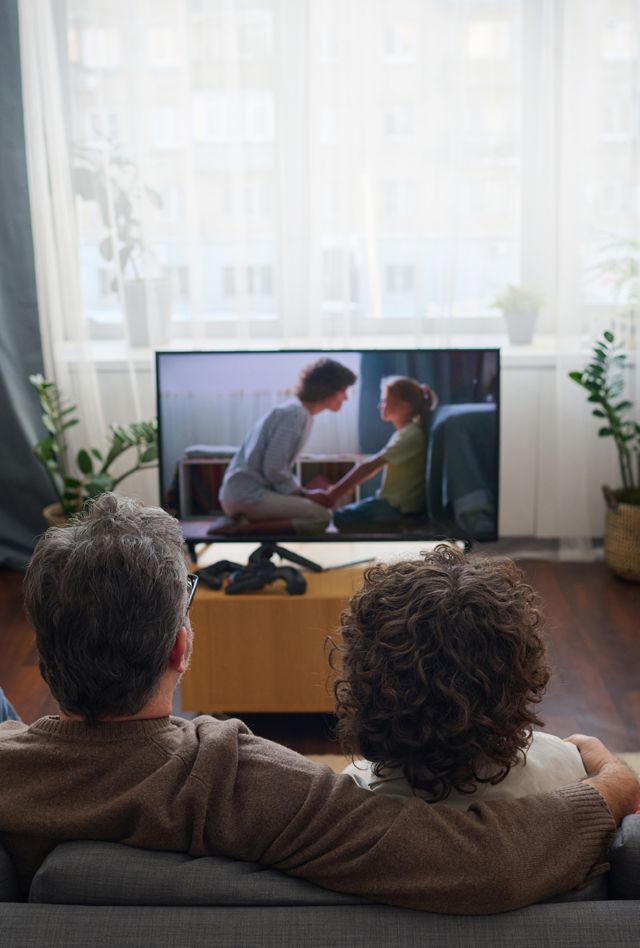 Rear view of family of four sitting together on sofa and enjoying watching the movie
