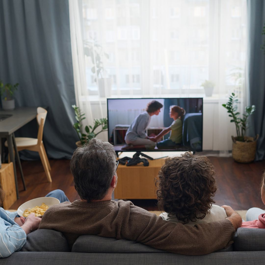 Rear view of family of four sitting together on sofa watching a movie