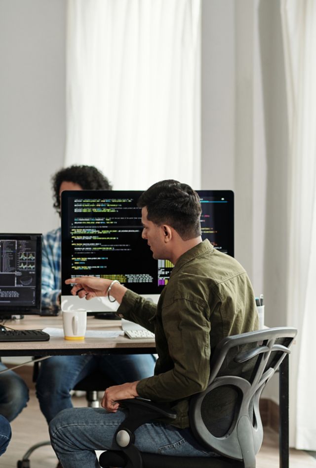 Four people sit at a table in front of computers displaying programming code