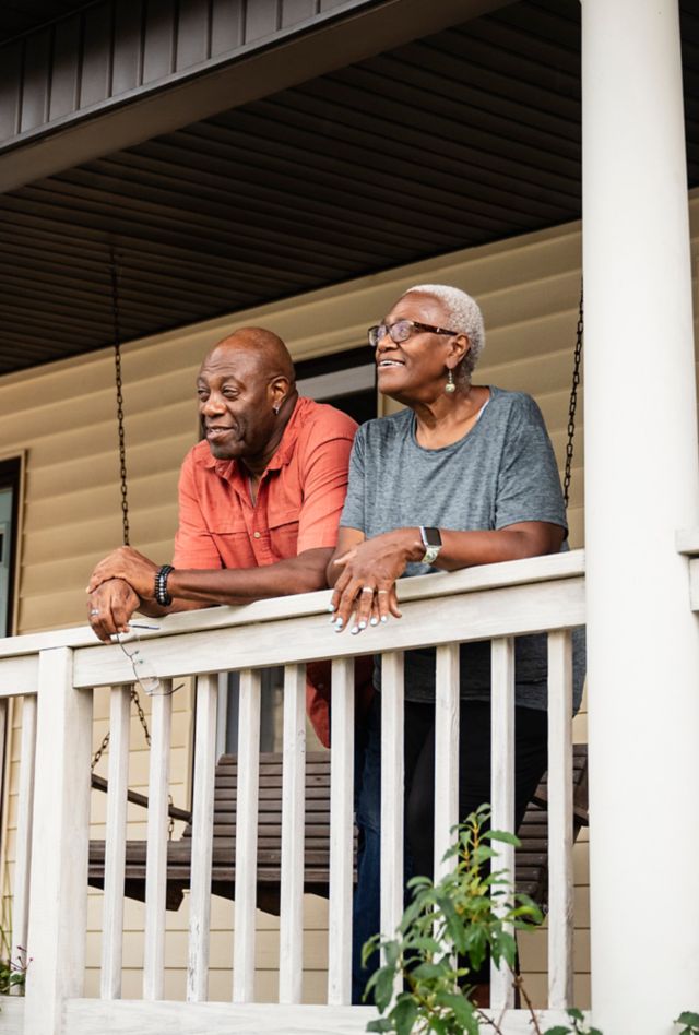 Older man and woman leaning on the railing of a porch and smiling