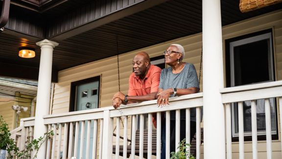 Older man and woman leaning on the railing of a porch and smiling