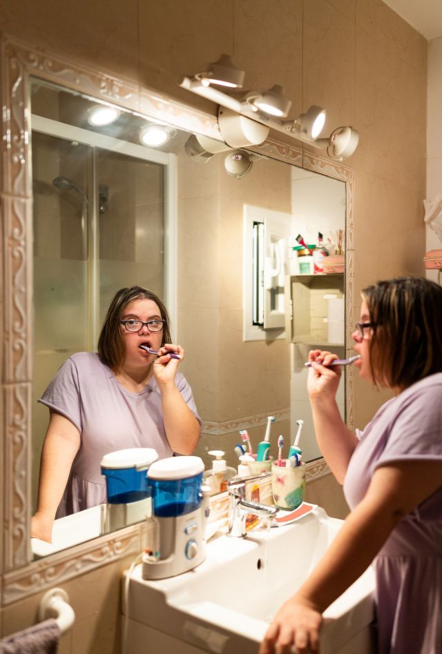 Vertical photo of the image reflected on a mirror of a woman with down syndrome cleaning her teeth in the bathroom