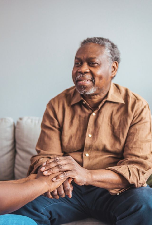 Close-up of health care worker and senior woman holding hands, both African American