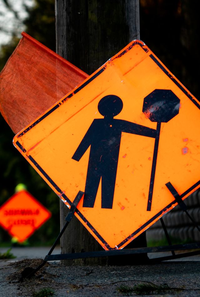 Lane closure on a busy road due to maintenance signs detour traffic temporary street work orange lighted arrow, barrels, and cones.