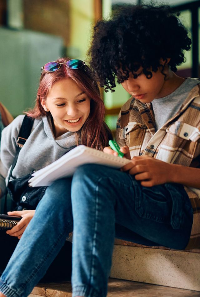 Happy teenager girl using laptop while studying with her classmates at high school.