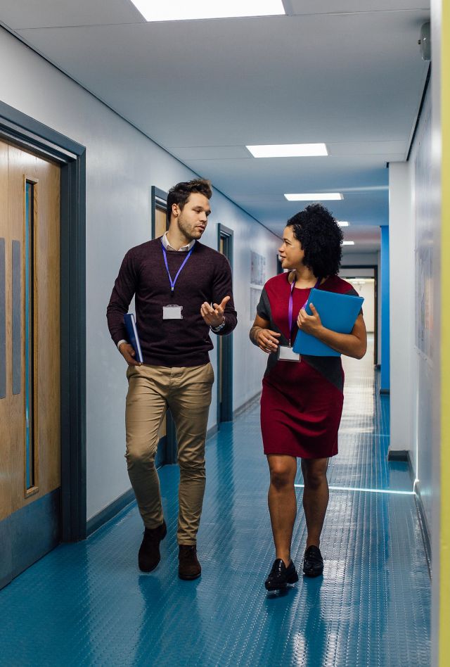 Two professionals talk as they walk down a hallway