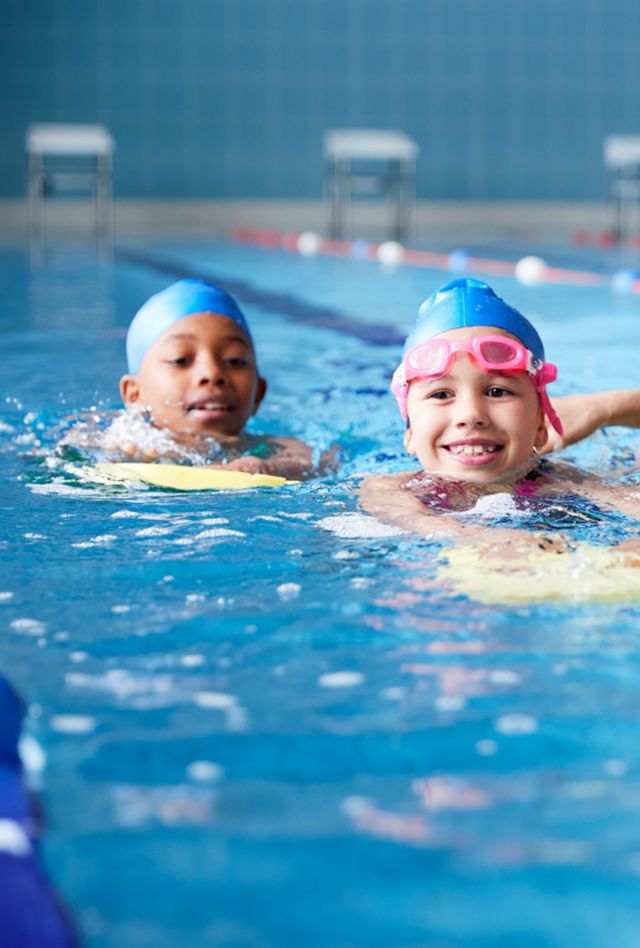Female Coach In Water Giving Group Of Children Swimming Lesson In Indoor Pool