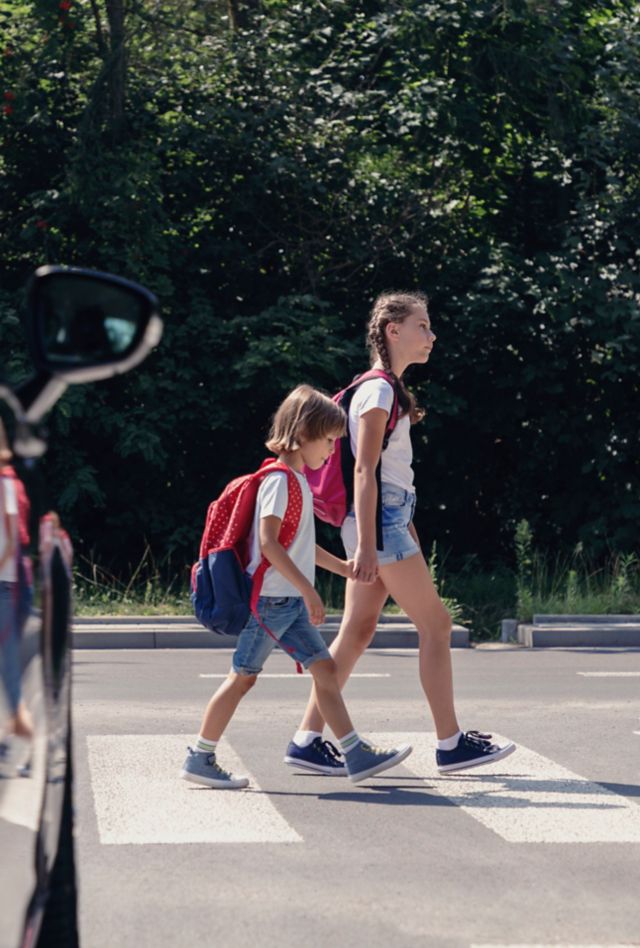 Children next to a car walking through pedestrian crossing to the school