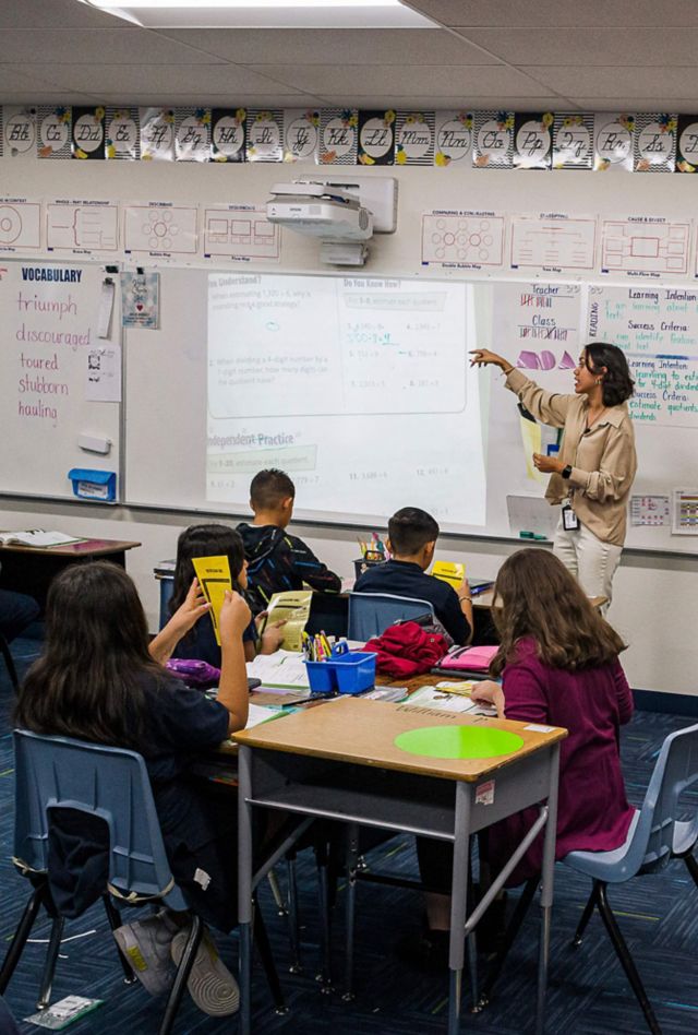 Teacher at white board in elementary school classroom while another teacher looks on