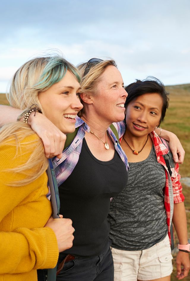A group of happy and positive female hiking friends huddle together on a rocky moorland in an idyllic rural countryside.