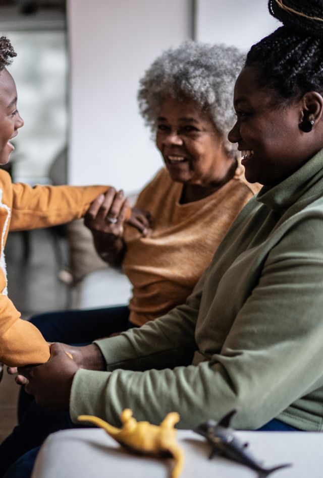 Child wearing a hearing aid playing with his mother and grandmother in the living room at home