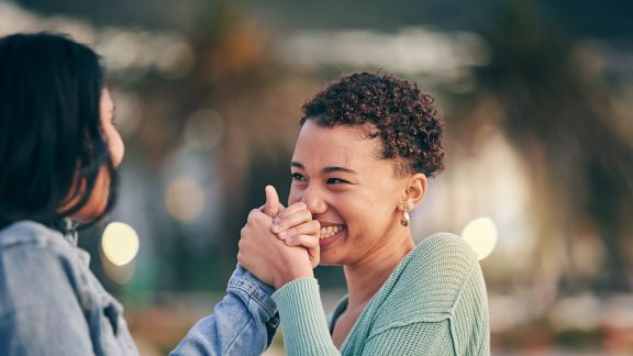 Two teens clasping hands as they look at each other and laugh