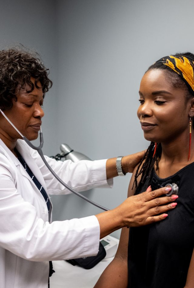 a Stock photo of a young African American woman being seen by her medical Cannabis doctor for her yearly checkup and consultation. In this image, the doctor is using her stethoscope to check to see how the patient is doing with her medication.
