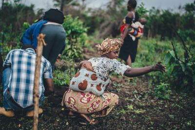 Dark-skinned men and women with babies tied to their backs in a field.