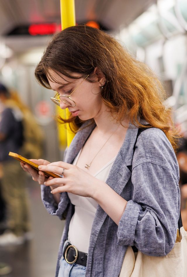 Young woman looks at her phone while standing in a subway car