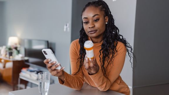 A woman holding a smartphone and a prescription pill bottle