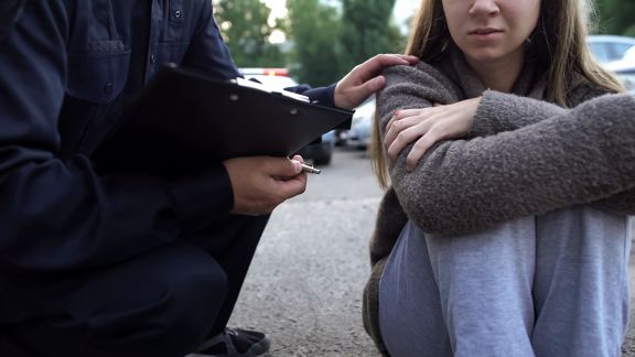 Officer trying to calm down female victim of car accident, shocked girl crying