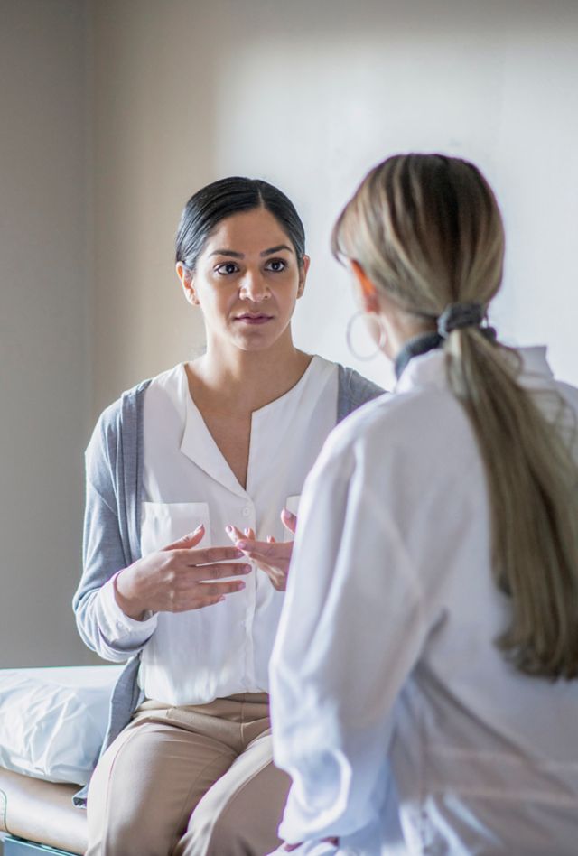 A woman sits on the examination table at the doctor's office during an exam.