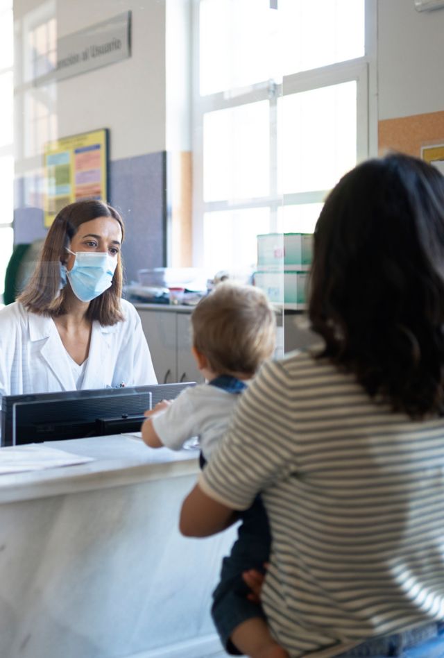 Receptionist in a doctor's office talks to a woman holding a baby