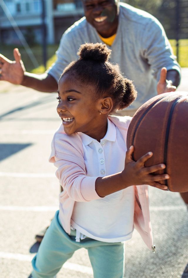 Close up of an older man playing basketball with a young girl in a park