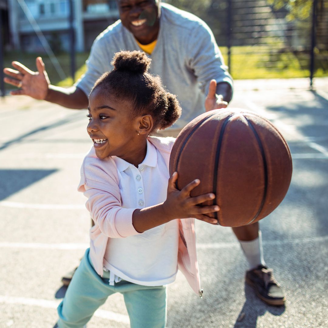Close up of an adult man playing basketball with a young girl in an outdoor basketball court