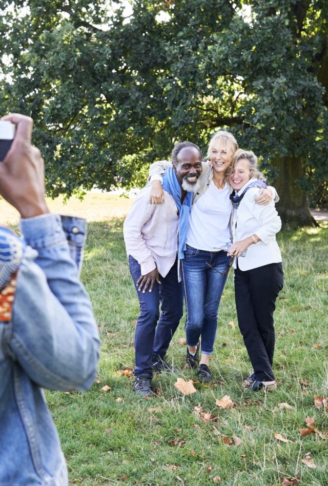 Faceless african rastafarian female taking group photo of friends at park.