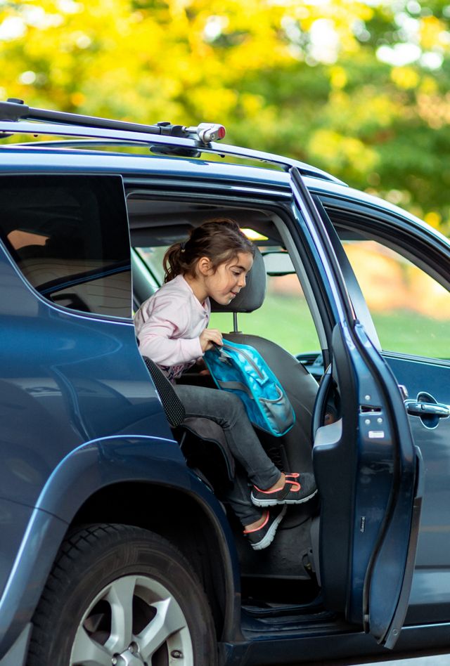 Young and excited kindergarten aged girl of multiracial ethnicity climbs out of a silver colored vehicle as her father drops her off on her first day of school.