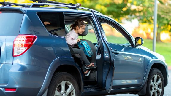 Young girl climbs out of the back seat of a silver colored vehicle