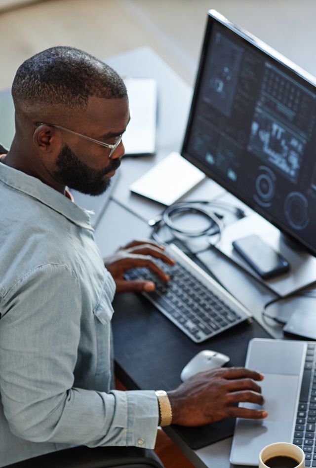 Minimal high angle view at African American software developer working with computers and data systems in office
