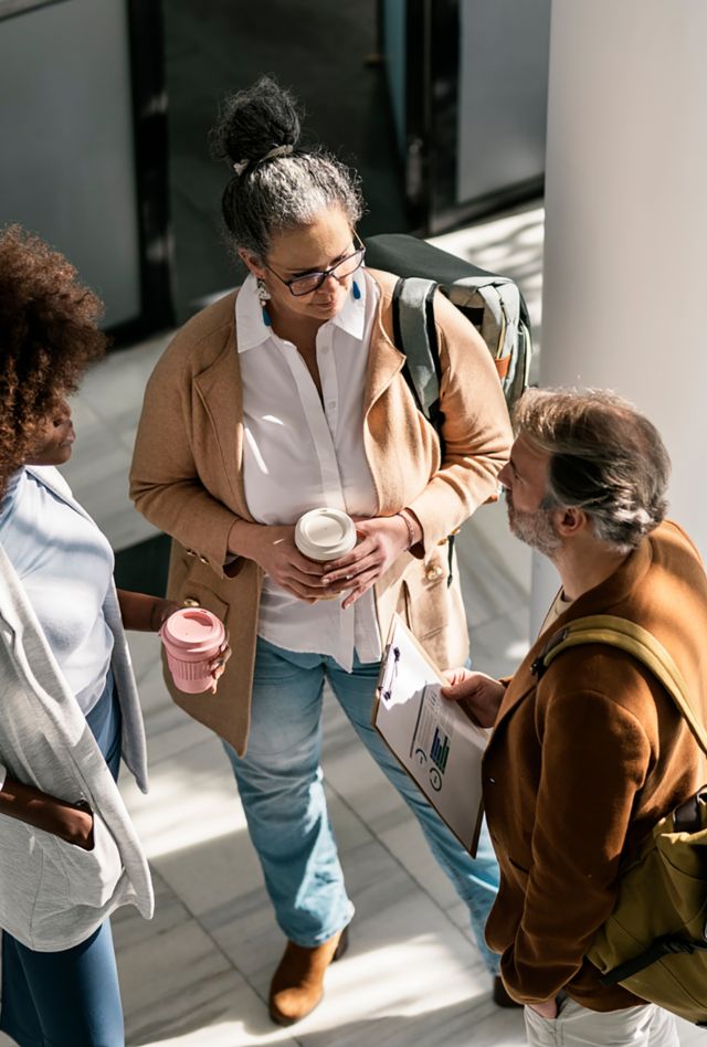 Top view of diverse male and female coworkers in smart casual clothes drinking takeaway coffee and talking during discussion of business plan in modern office