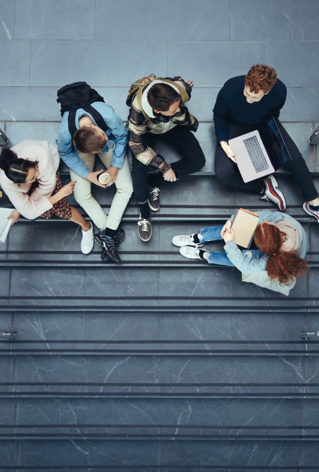 Young people at college during break time. Boys and girls sitting on stairs in university campus.