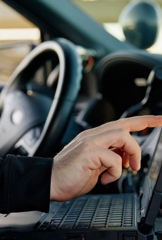 View of the interior of a police car, where a police officer sitting in the driving seat is using a laptop.
