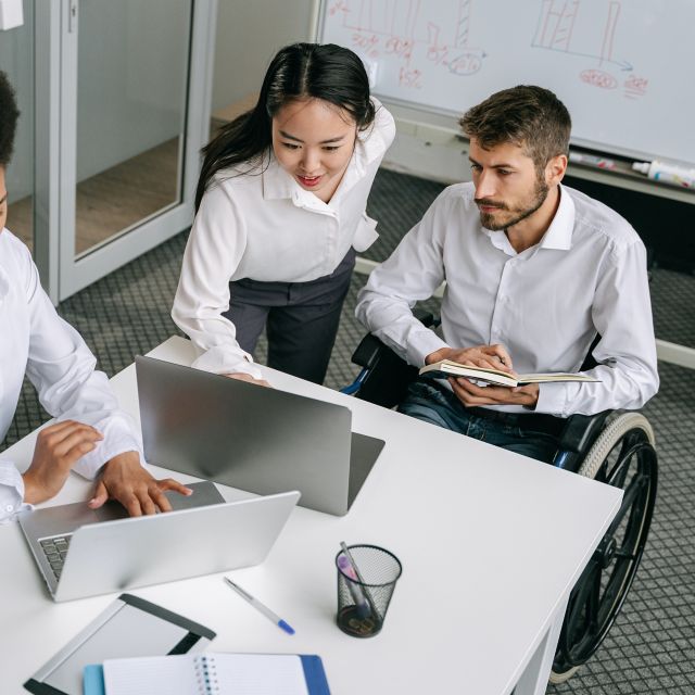 Group of diverse young professionals around a table looking at a laptop