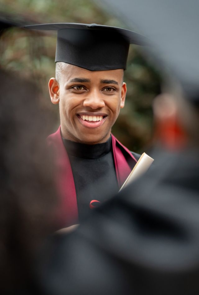 African American student looking wearing a graduation cap and robe and smiling