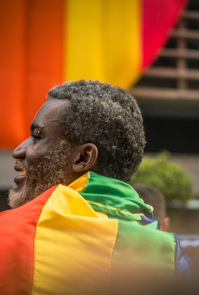 A Black individual with a rainbow flag wrapped around them at a pride parade