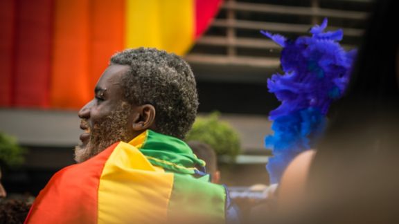 A Black individual with a rainbow flag wrapped around them at a pride parade