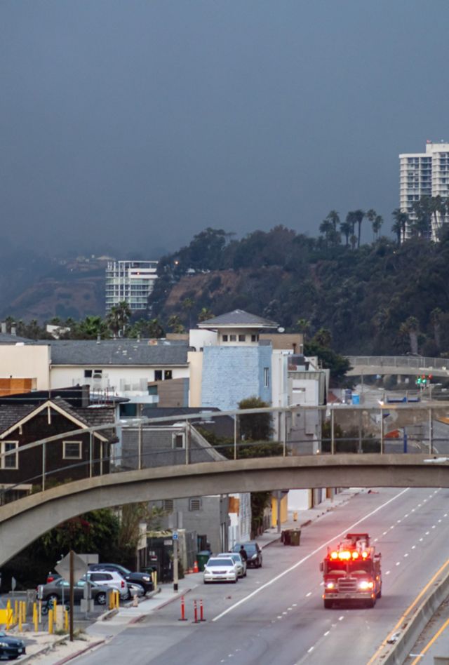 Los Angeles, California, USA. January 8th, 2025. Plumes of smoke drift over a fire truck driving along the Pacific Coast Highway or PCH as the Pacific Palisades fire and Eaton fire burn near Los Angeles, California.