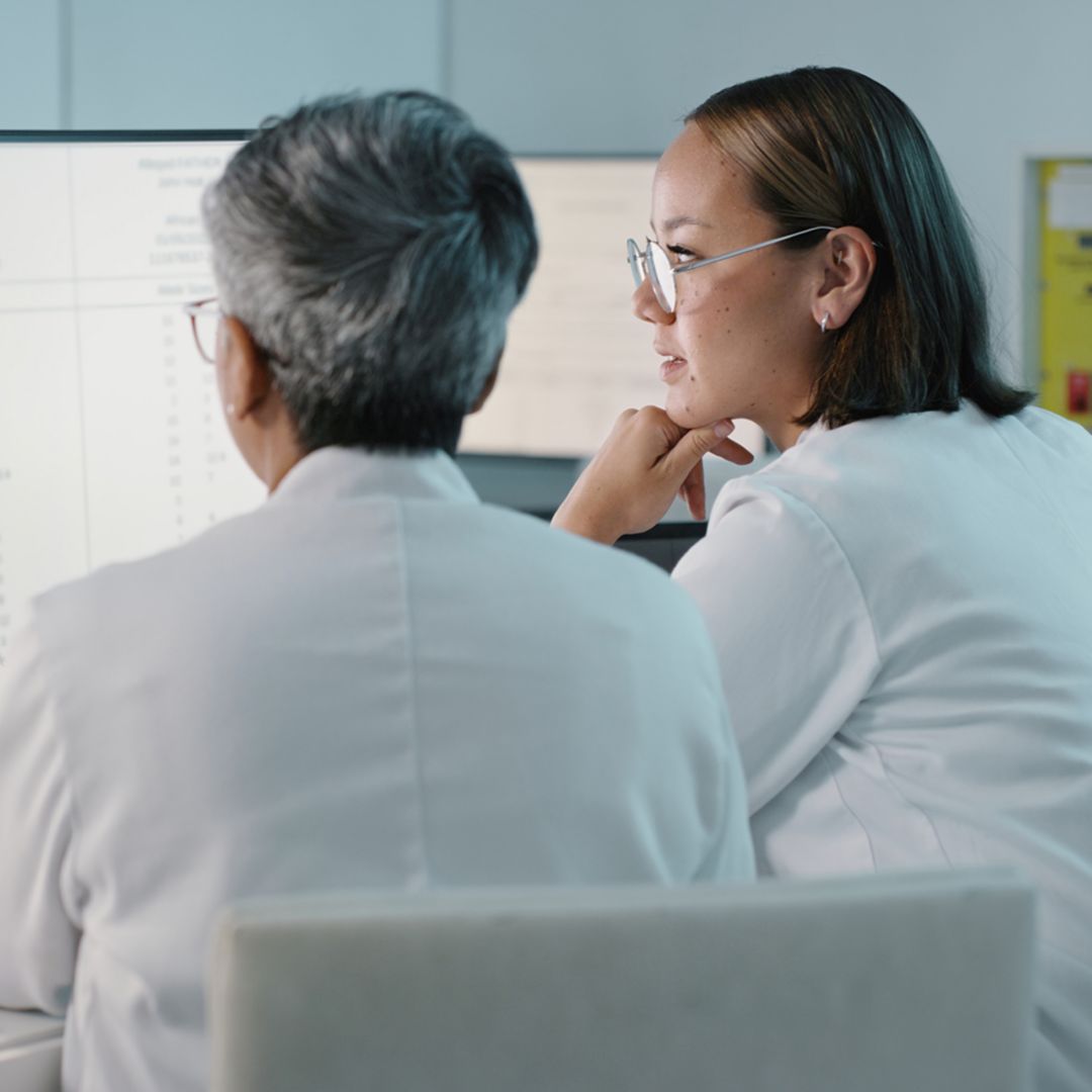 Two people in white lab coats working at a computer