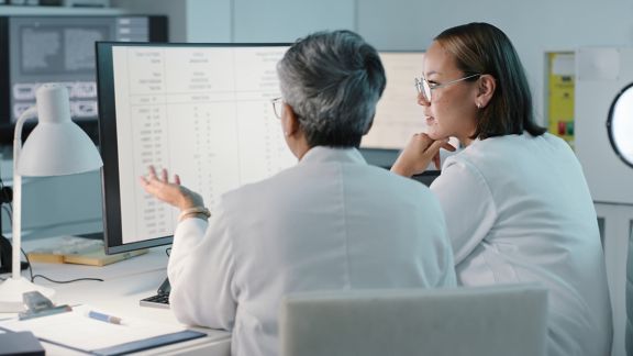Two people in white lab coats working at a computer