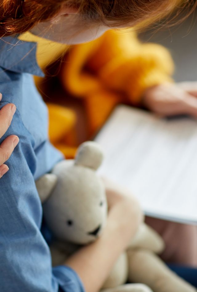 Closeup of a teenage girl's shoulder with an unrecognizable woman's hand caringly holding it.