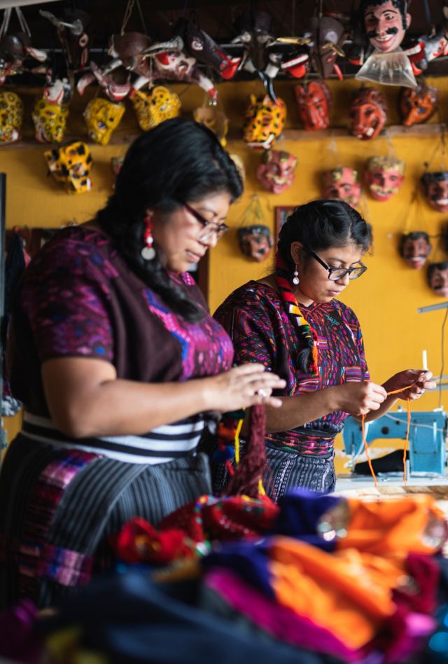 Stock photos of beautiful Guatemalan women in a small workshop using a sewing machine creating masks, costumes and colorful traditional clothing. Small businesswomen in their handicraft workshop.