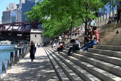 Chicago skyline in background, people sitting on steps near river 