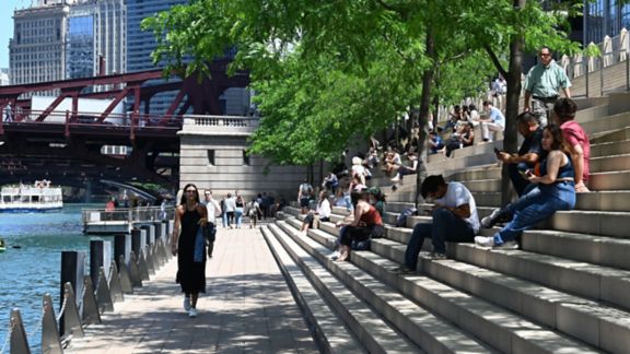 Chicago skyline in background, people sitting under the shade of trees on the steps by the river